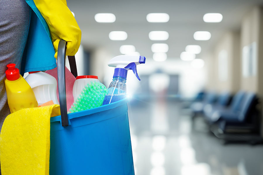 Cleaning woman with bucket and cleaning supplies on blurred background of hospital or office corridor.